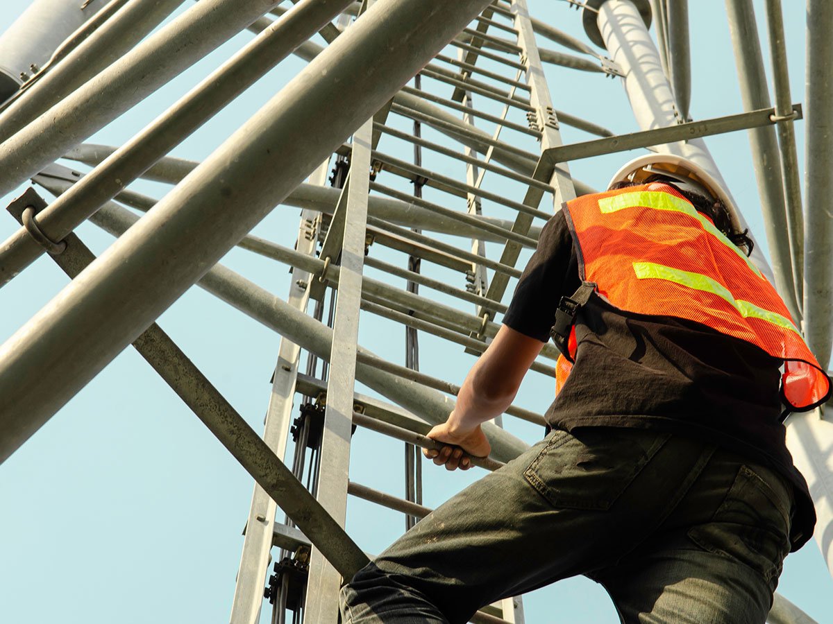 photo of a man in a high-vis technician vest climbing a tower. low perspective.